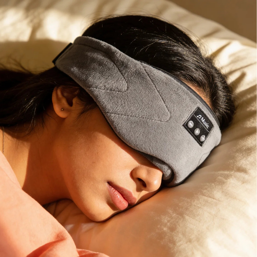 The Qullaby DreamWave sleep mask resting on bedding in soft light